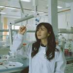 Student in a lab in a white lab coat looking at a bacterial plate