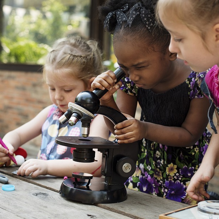 three young children looking through a microscope