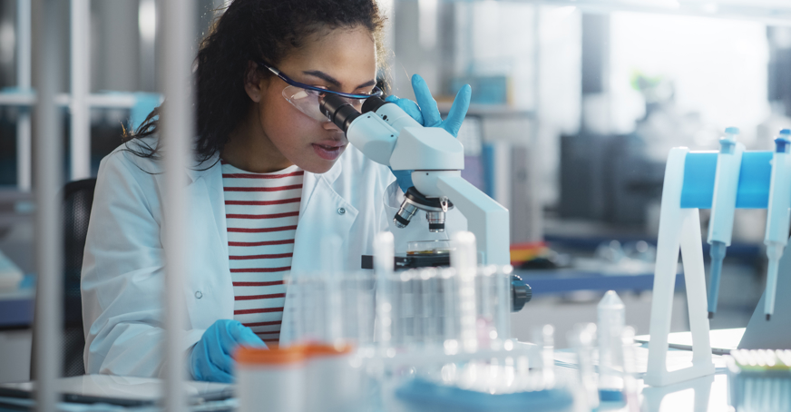 A molecular bioscientist looking through a microscope in a lab